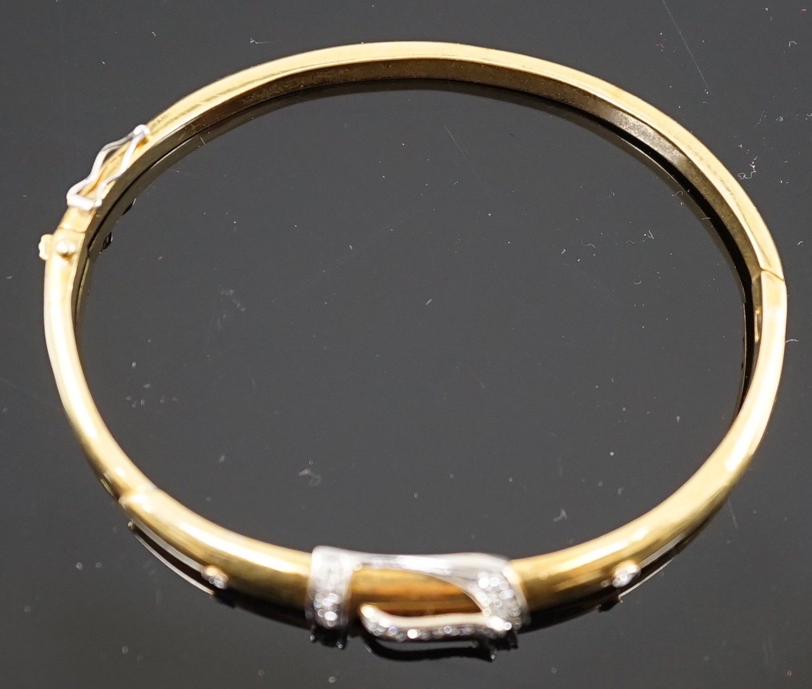 A gold and diamond set hinged bangle with central buckle motif